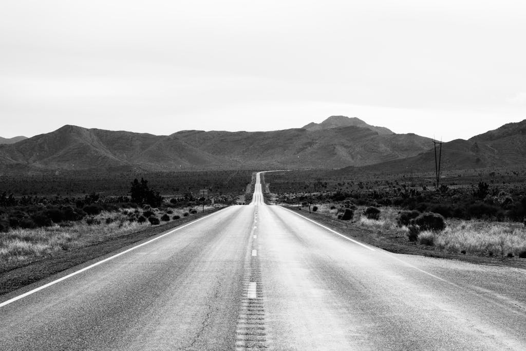 Black and white image of an endless road through desert mountains, offering a scenic travel view.