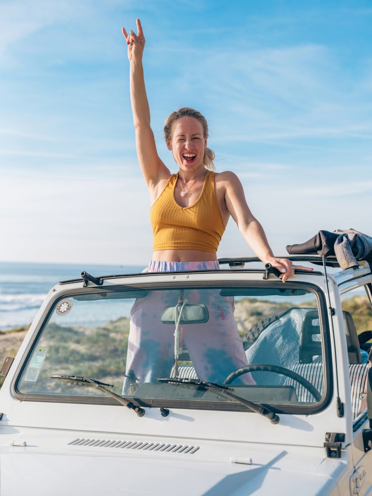 Smiling woman standing in a convertible car near the ocean, celebrating and having fun in Lisbon.