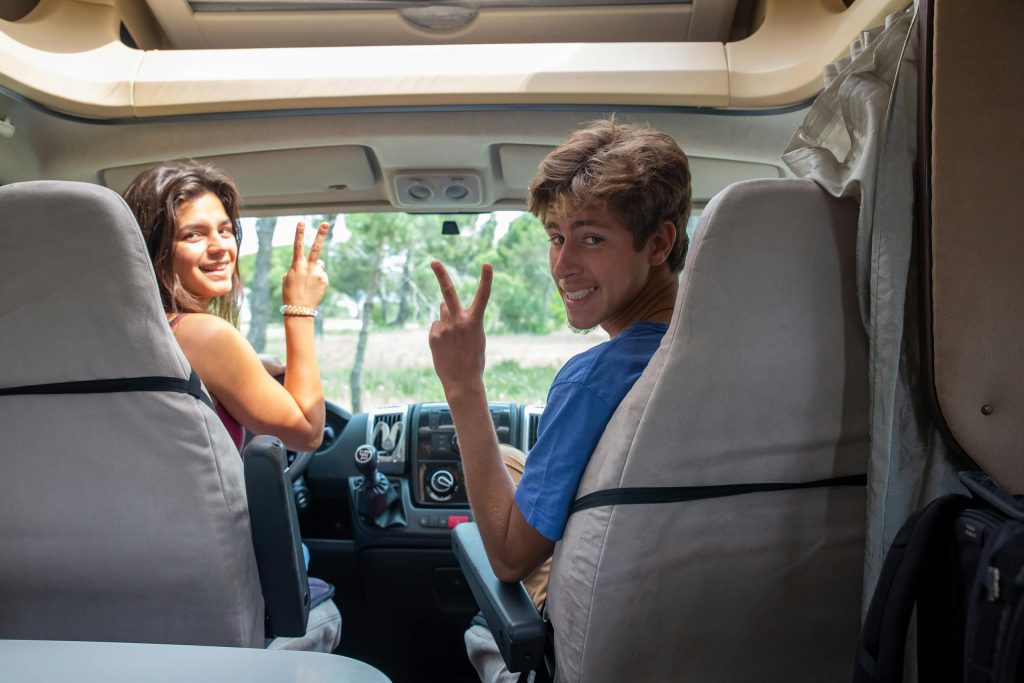 Happy couple making peace signs during a sunny road trip in a camper van in Portugal.