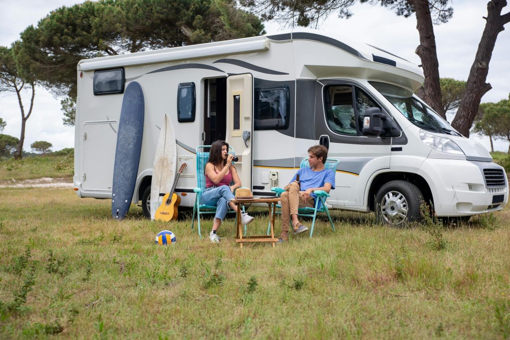 Young couple relaxing outside their RV with surfboards and guitar, enjoying a summer day in Portugal.