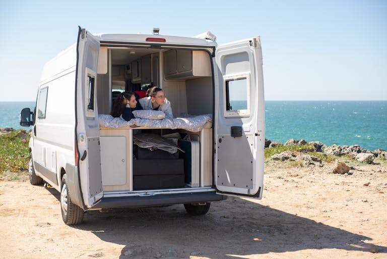 Couple enjoying a relaxing moment in their camper van by the scenic ocean view.