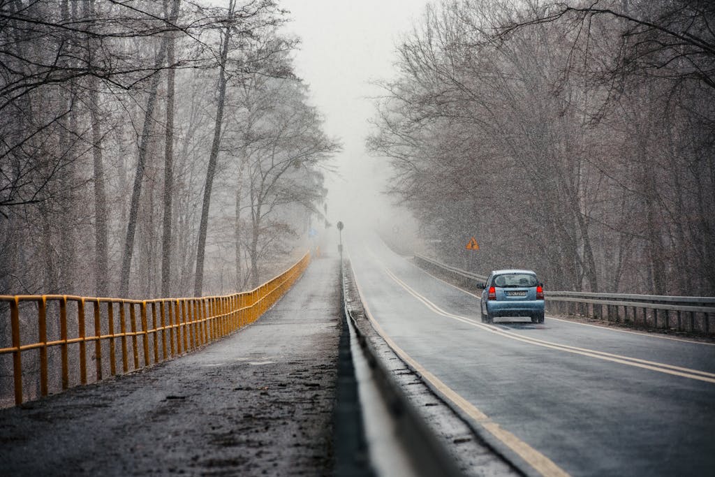 A scenic winter road in Konin, Poland with a single car, surrounded by trees.