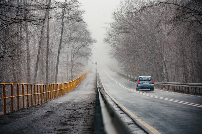 A scenic winter road in Konin, Poland with a single car, surrounded by trees.