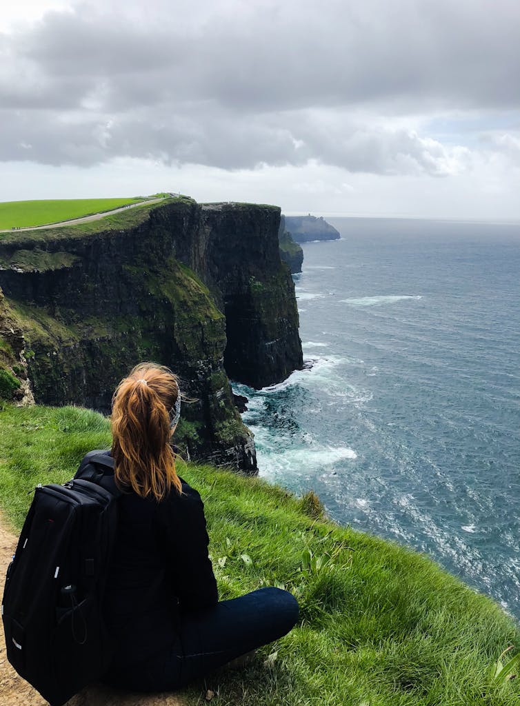 Woman sitting and admiring the stunning Cliffs of Moher in County Clare, Ireland.