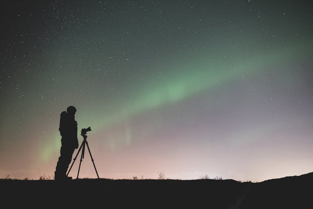 A silhouette of a photographer captures the stunning Northern Lights in Iceland's night sky.