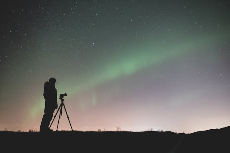 A silhouette of a photographer captures the stunning Northern Lights in Iceland's night sky.