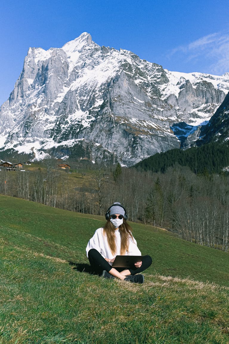 Woman working remotely on a laptop with a mountainous alpine backdrop.